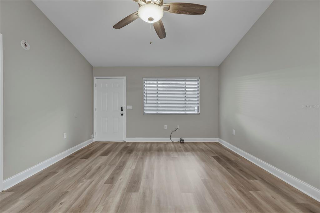 An empty room features light gray walls, wood-look flooring, a ceiling fan, and a window — 1203 SHADY PINES LANE, TITUSVILLE, FL