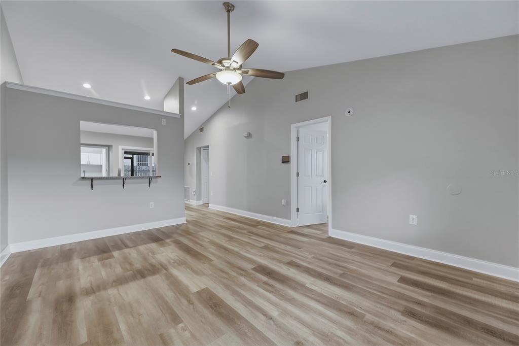 An empty living room features light wood-look flooring, vaulted ceilings, and a ceiling fan — 1203 SHADY PINES LANE, TITUSVILLE, FL