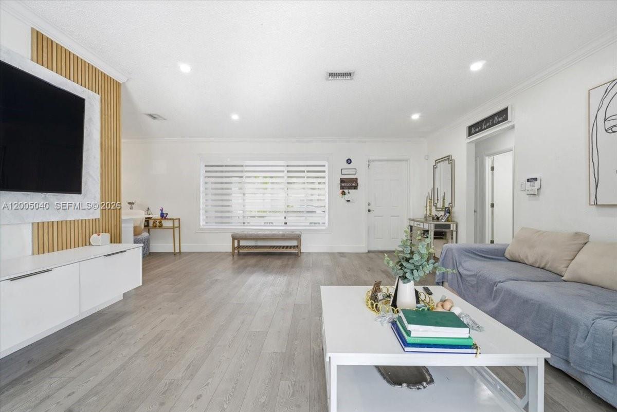 A bright living room features light wood-look flooring, a white media console, and a sofa — 740 SW 7th Ave, Hallandale Beach FL 33009, HALLANDALE BEACH, FL