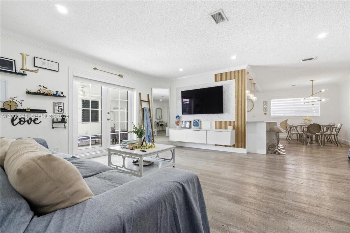 A living room features a wall-mounted television, wood slat accents, and an adjacent dining area — 740 SW 7th Ave, Hallandale Beach FL 33009, HALLANDALE BEACH, FL