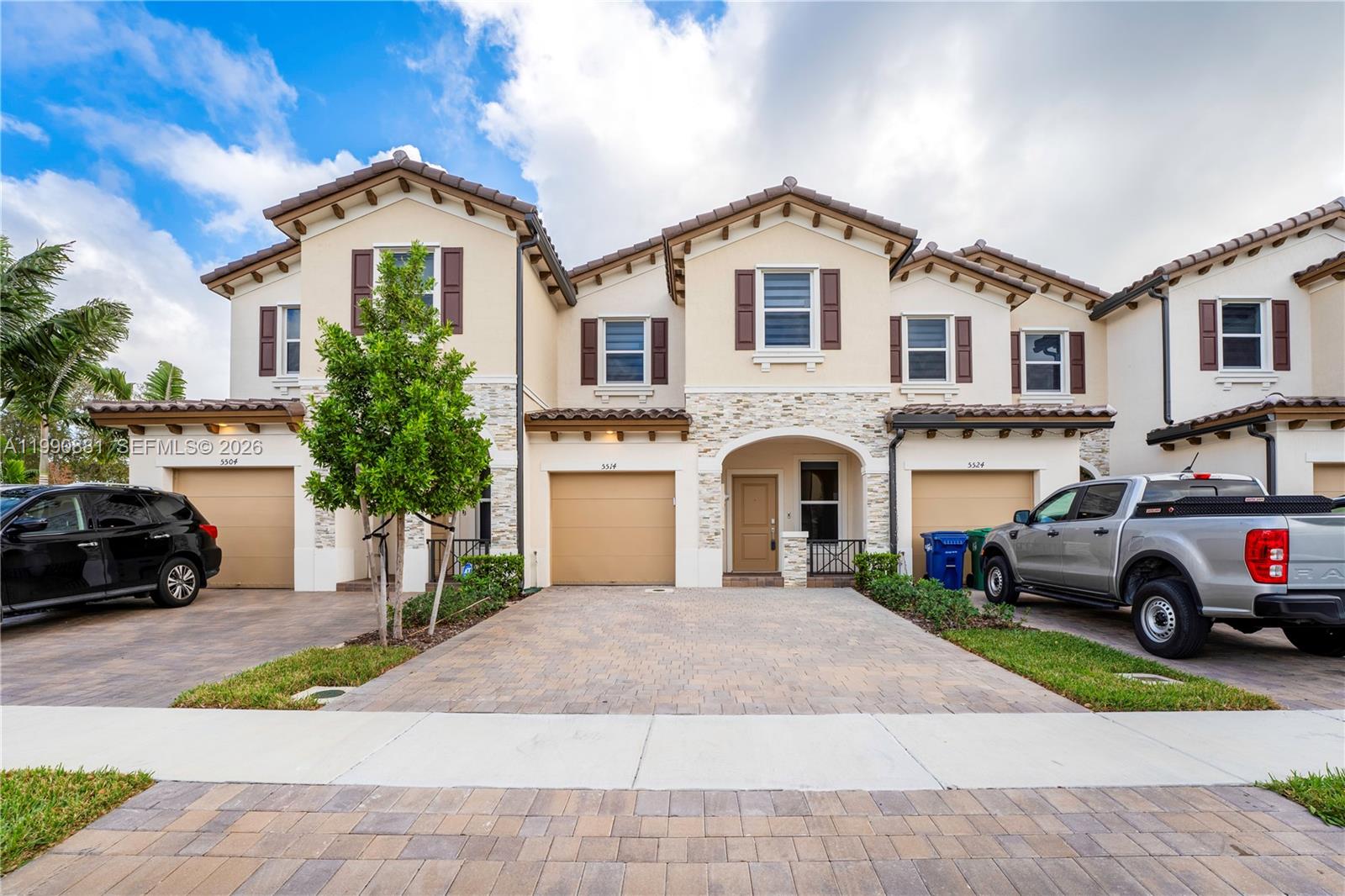 A row of three two-story townhouses with beige stucco, stone accents, and paved driveways — 5514 NW 27th St, Lauderhill FL 33313, LAUDERHILL, FL