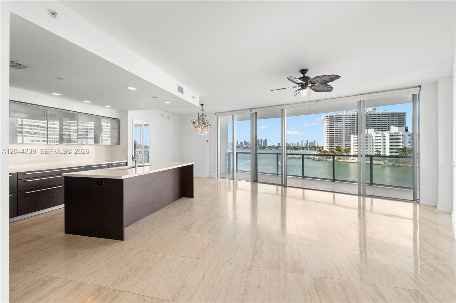 A modern kitchen with a dark island overlooks a balcony with water and city views — 1470 16th St # 401, Miami Beach FL 33139, MIAMI BEACH, FL