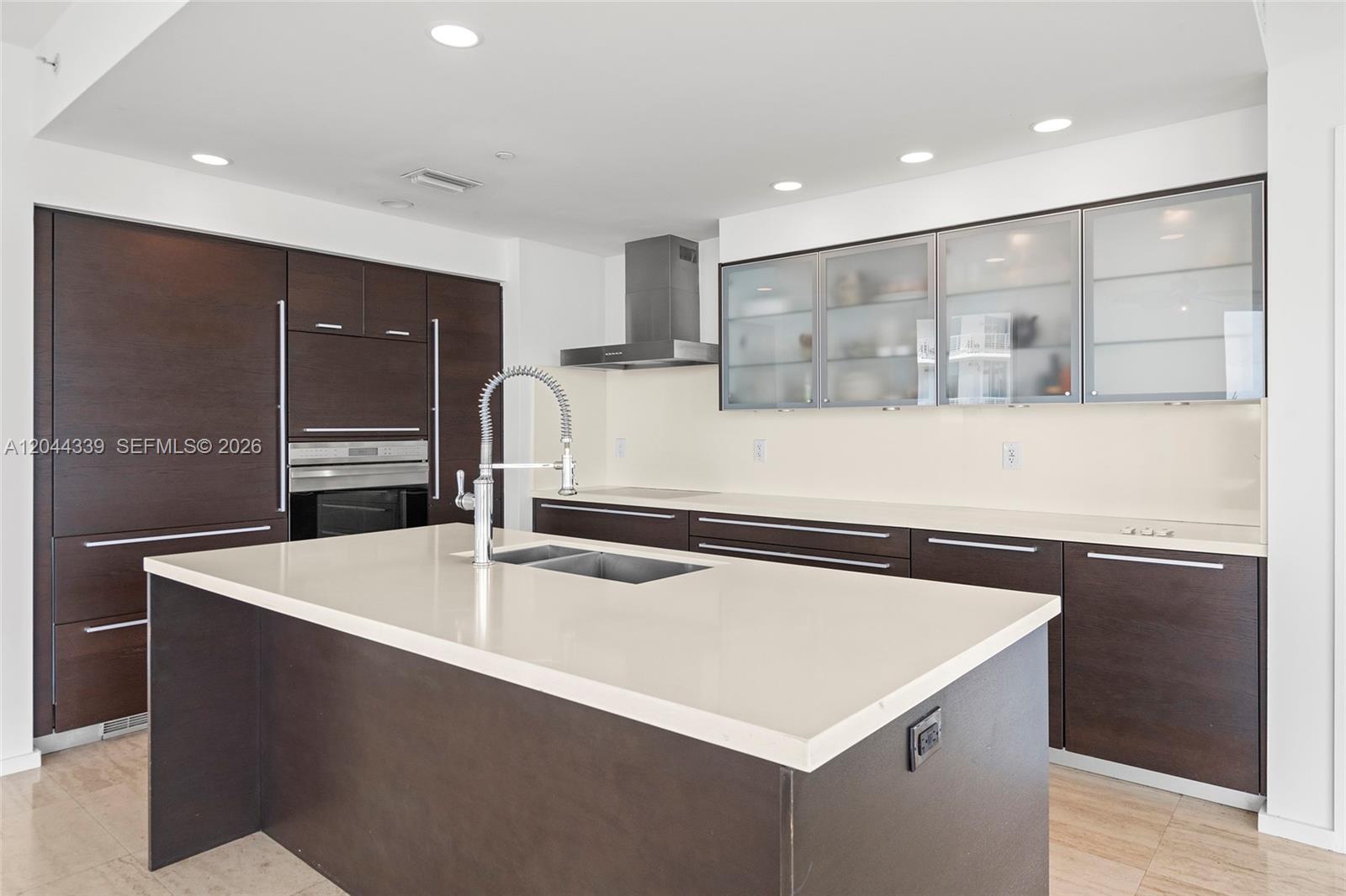 A modern kitchen features dark wood cabinetry, a large white island, and stainless steel appliances — 1470 16th St # 401, Miami Beach FL 33139, MIAMI BEACH, FL