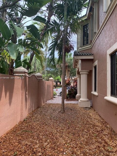 A narrow side yard features a gravel ground cover, a palm tree, and stucco walls — 2800 Kinsington Cir, Weston FL 33332, WESTON, FL