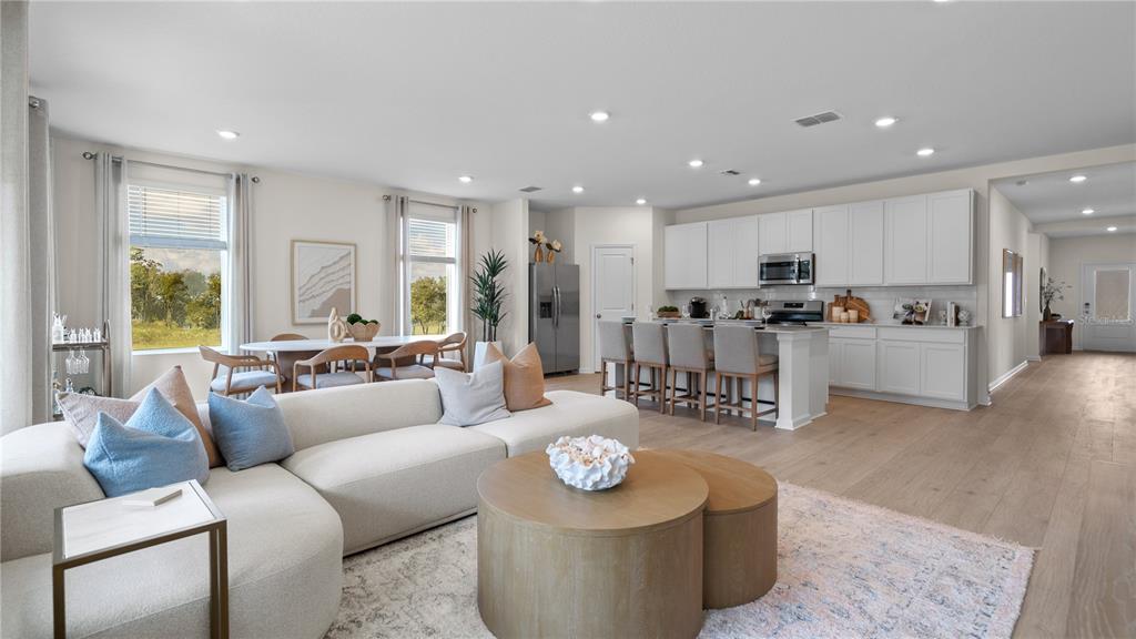 An open-concept living room and kitchen feature light wood floors, white cabinetry, and neutral furniture — 3235 MINDFULLNESS DRIVE, CLERMONT, FL