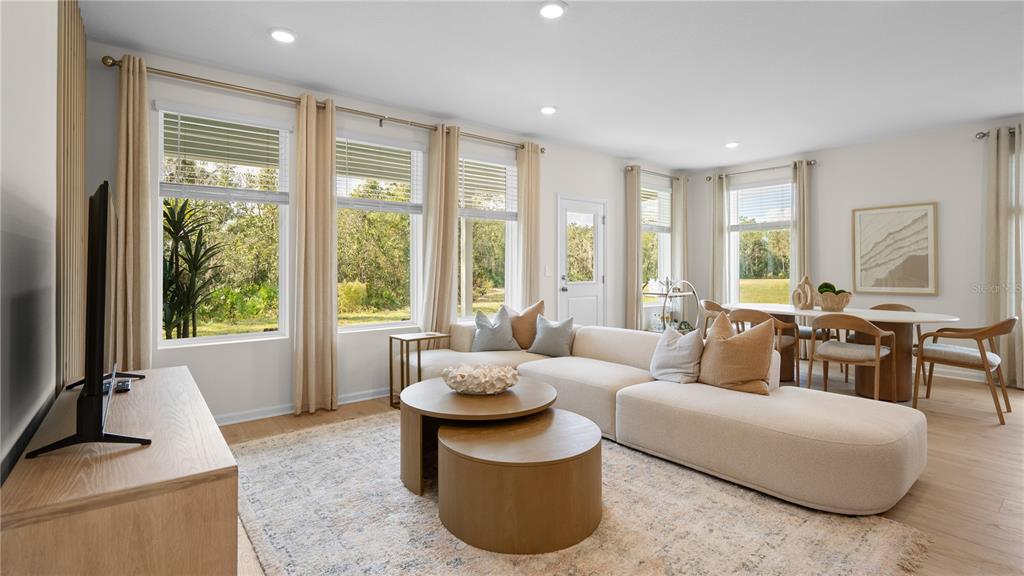 A bright living room features a beige sectional sofa, round wooden coffee tables, and large windows — 3235 MINDFULLNESS DRIVE, CLERMONT, FL
