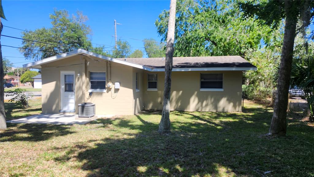 The exterior of a single-story tan house features a concrete patio and a central air unit — 565 3RD AVENUE, DAYTONA BEACH, FL
