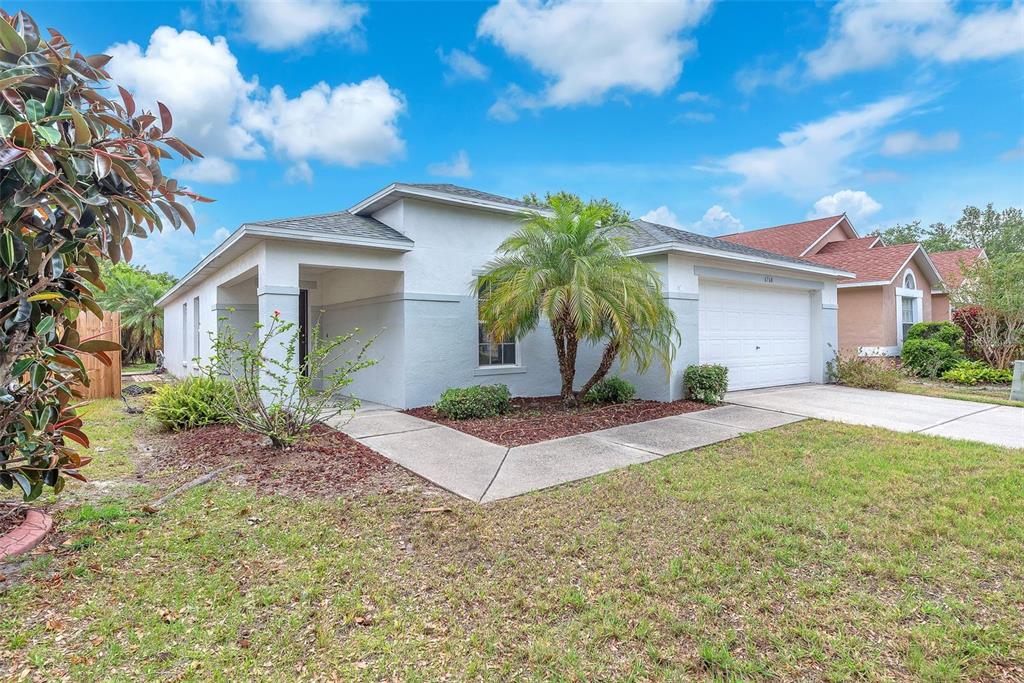 A single-story house with a white garage, gray stucco exterior, and a small palm tree — 6760 WATERTON DRIVE, RIVERVIEW, FL