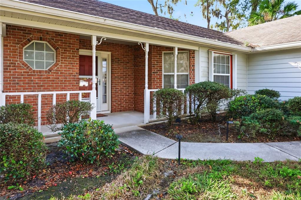 A brick house exterior features a covered porch, white railings, and a concrete walkway — 905 NORTHERN OAKS TERRACE, DELAND, FL