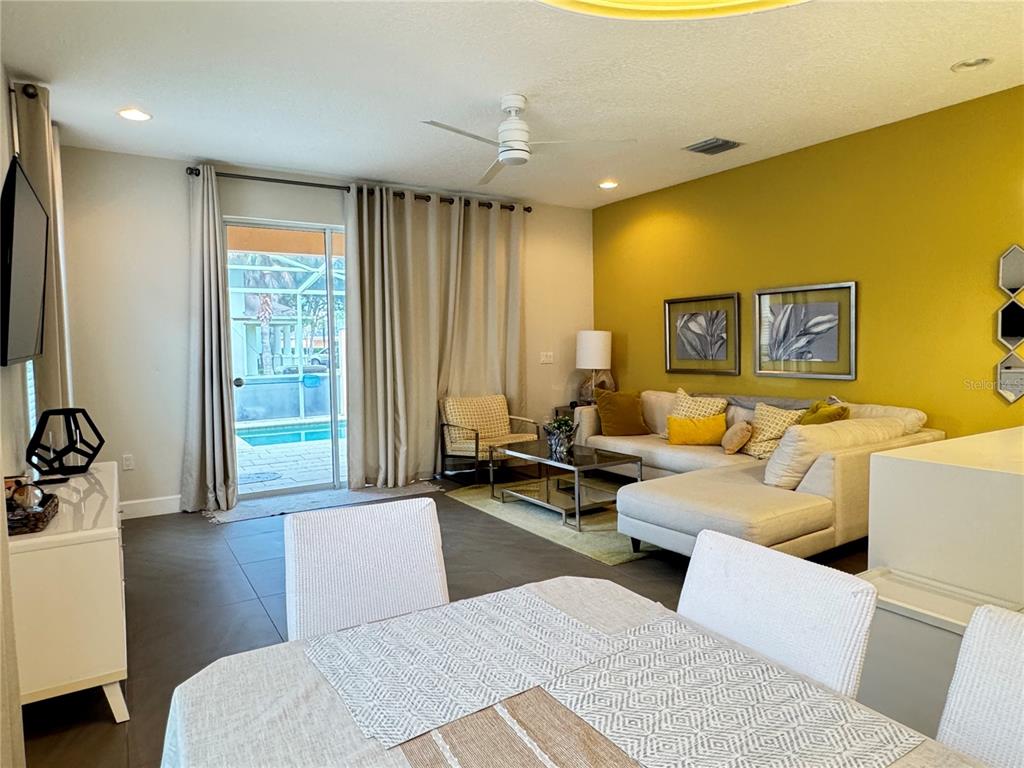 A living room with a yellow accent wall, sectional sofa, and sliding doors to a pool — 17343 SERENIDAD BLVD, CLERMONT, FL