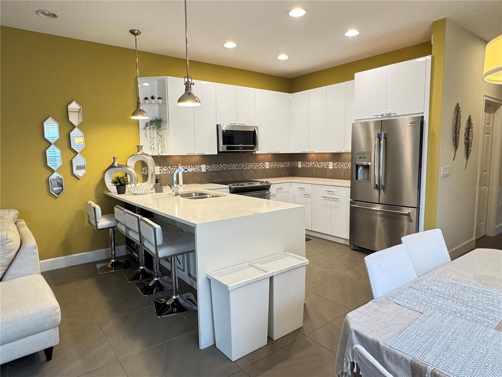 A modern kitchen features white cabinets, a quartz island with bar seating, and yellow walls — 17343 SERENIDAD BLVD, CLERMONT, FL