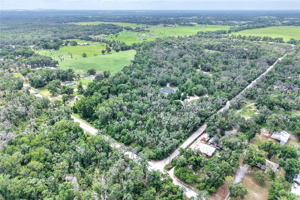 An aerial view shows a rural landscape with dense trees, open fields, and gravel roads — 600 THOMPSON ROAD, LITHIA, FL
