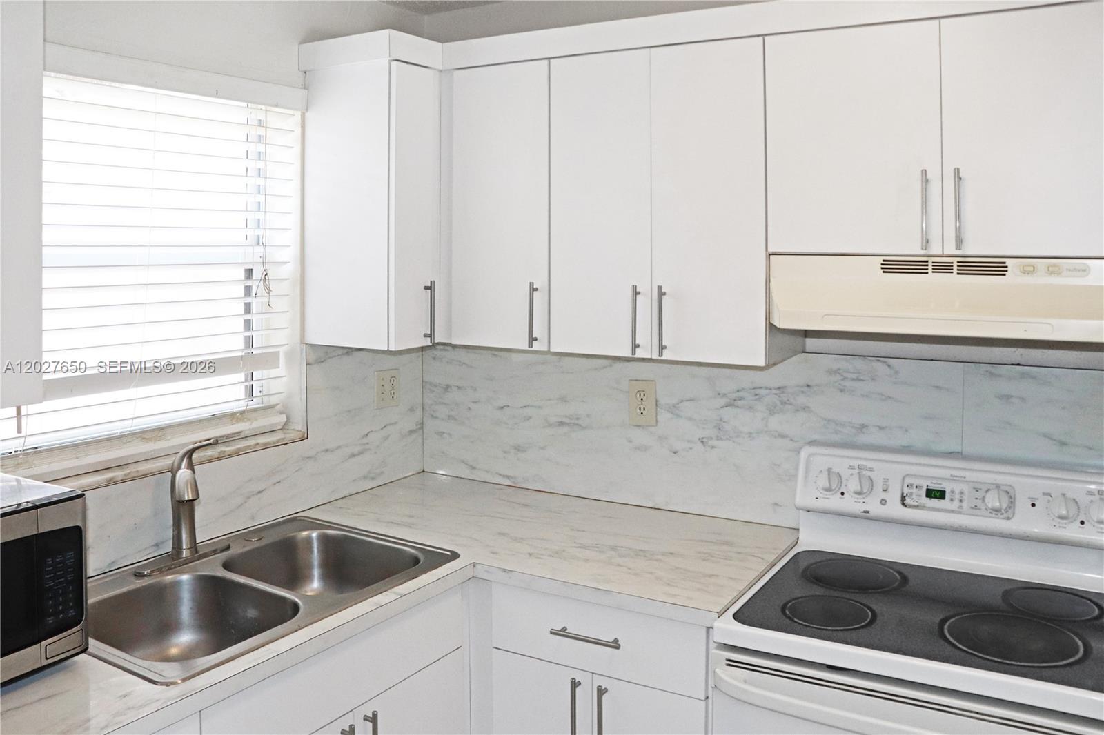 A kitchen features white cabinets, a marble-patterned backsplash, a double sink, and a white stove — 15006 SW 80th Ter # 913, Miami FL 33193, MIAMI, FL