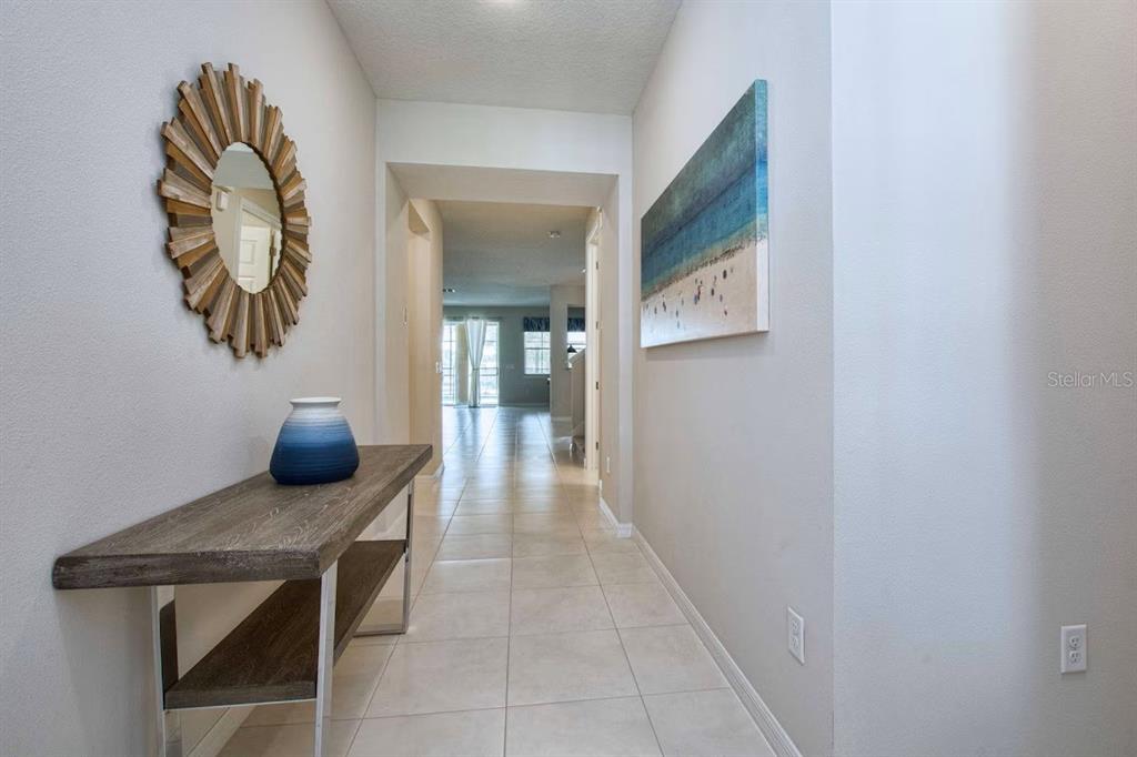 A hallway with tile flooring, a console table, a sunburst mirror, and a coastal wall painting — 9013 SUNSHINE RIDGE LOOP, KISSIMMEE, FL