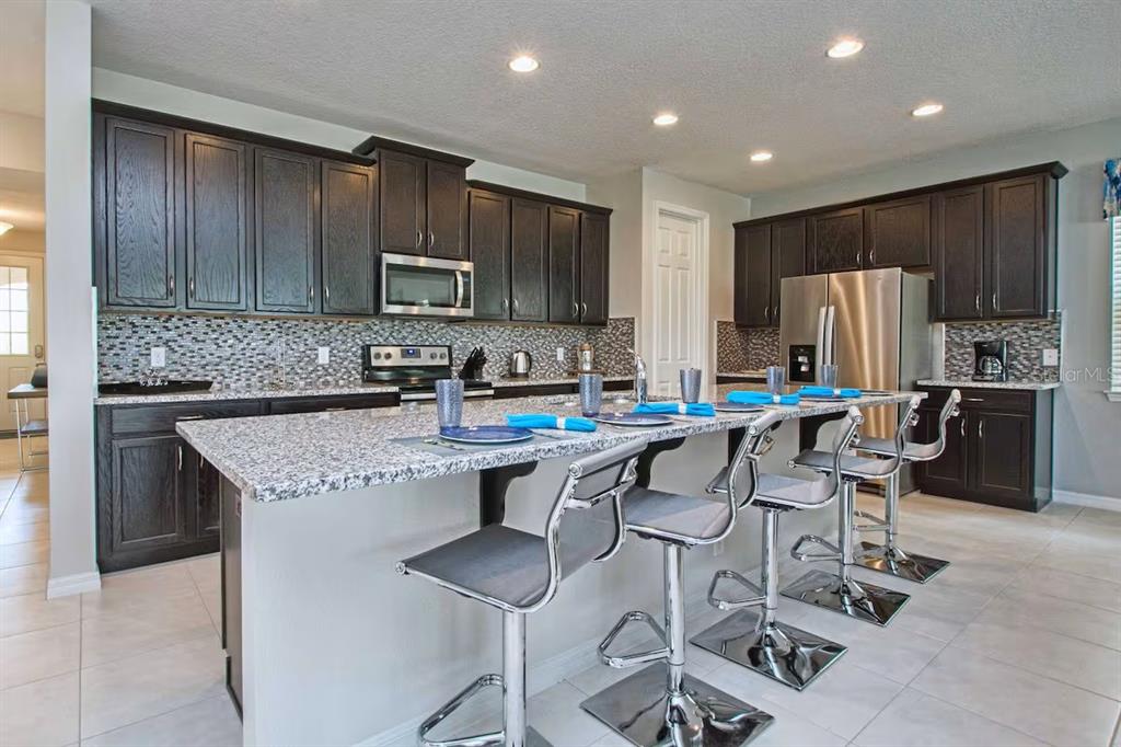 A kitchen features dark wood cabinets, granite countertops, a large island, and stainless steel appliances — 9013 SUNSHINE RIDGE LOOP, KISSIMMEE, FL
