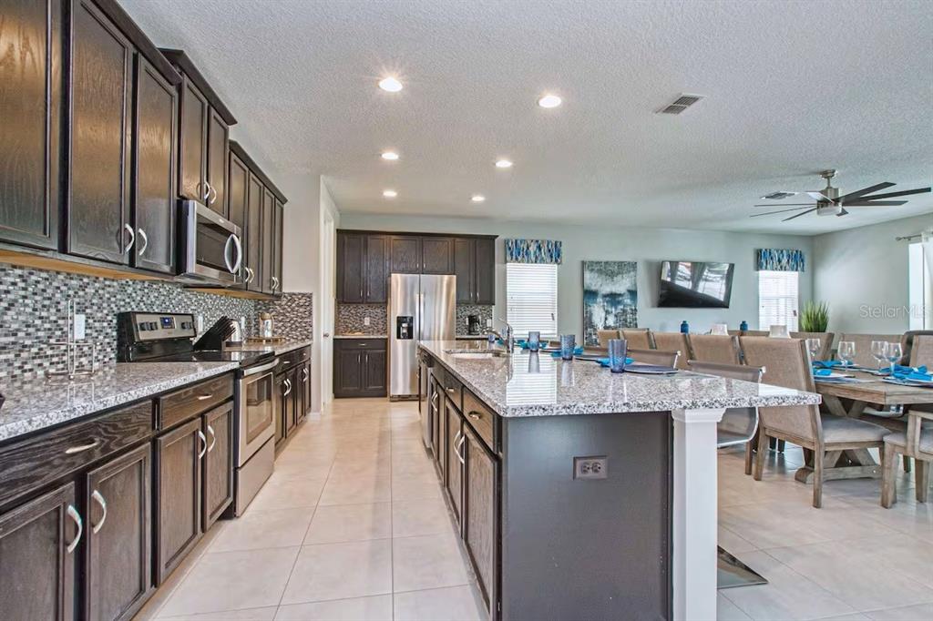 A kitchen with dark wood cabinets, granite countertops, a large island, and stainless steel appliances — 9013 SUNSHINE RIDGE LOOP, KISSIMMEE, FL