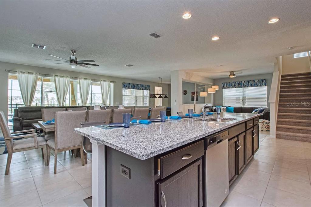 A kitchen island with granite countertops sits in an open-concept living and dining area — 9013 SUNSHINE RIDGE LOOP, KISSIMMEE, FL