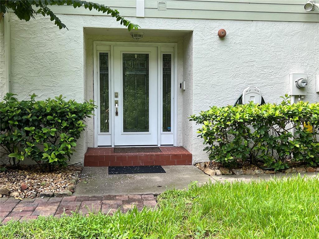 A white front door with sidelights is set into a stucco exterior with surrounding landscaping — 1383 CURLEW ROAD, DUNEDIN, FL