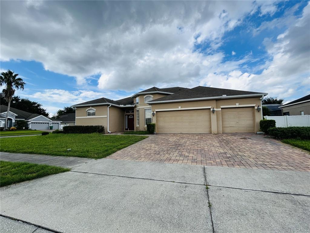 A single-story suburban house with a tan stucco exterior, a three-car garage, and a paver driveway — 1642 CHANDELLE LANE, WINTER GARDEN, FL
