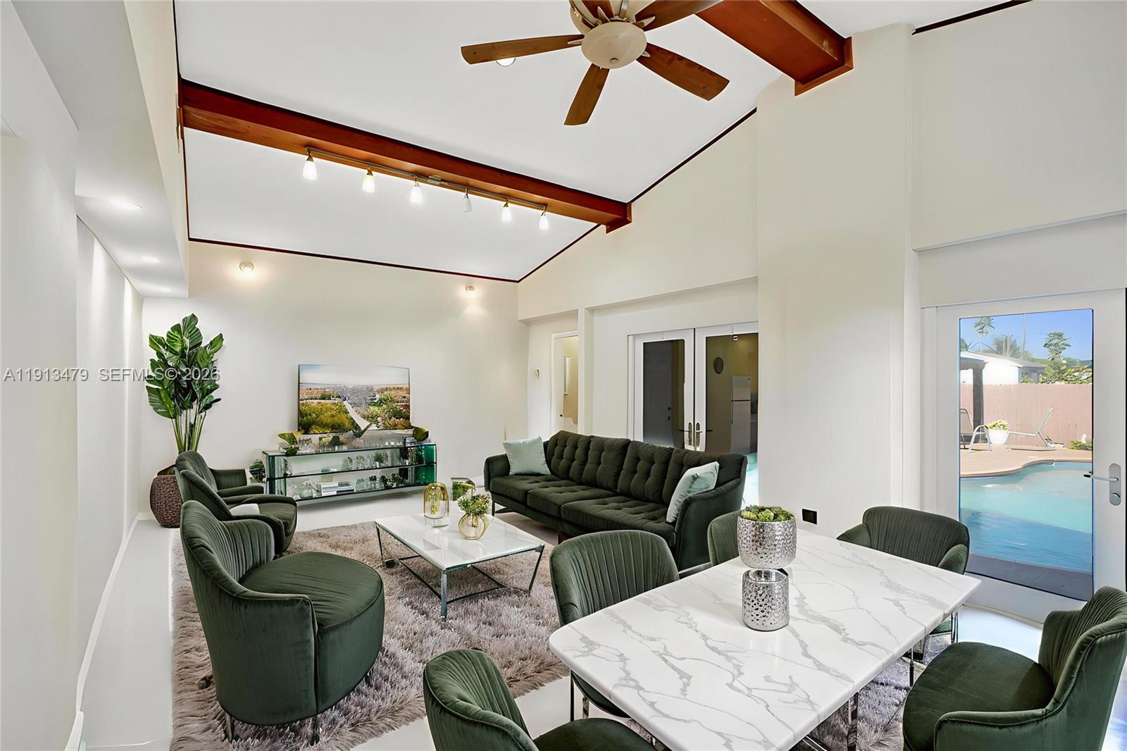 A living and dining area features vaulted ceilings with exposed beams, green furniture, and pool views — 311 E 51st St, Hialeah FL 33013, HIALEAH, FL