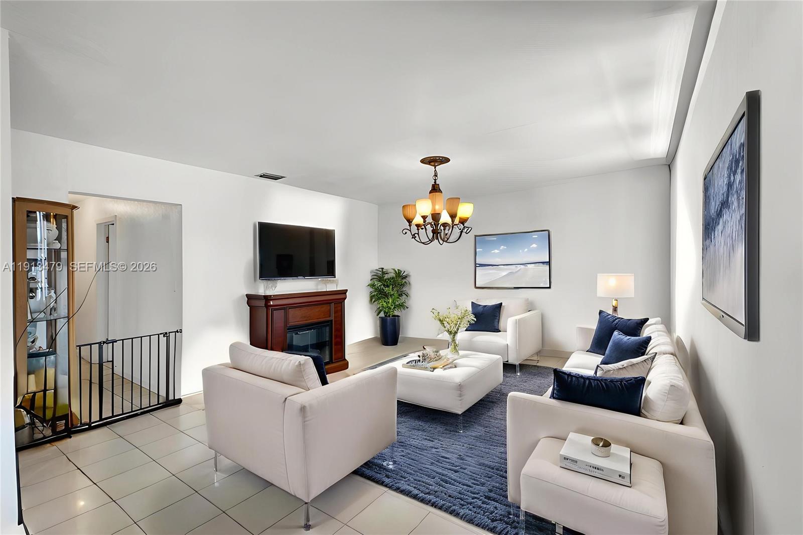 A living room features white furniture, a dark blue rug, and a fireplace with a television — 311 E 51st St, Hialeah FL 33013, HIALEAH, FL