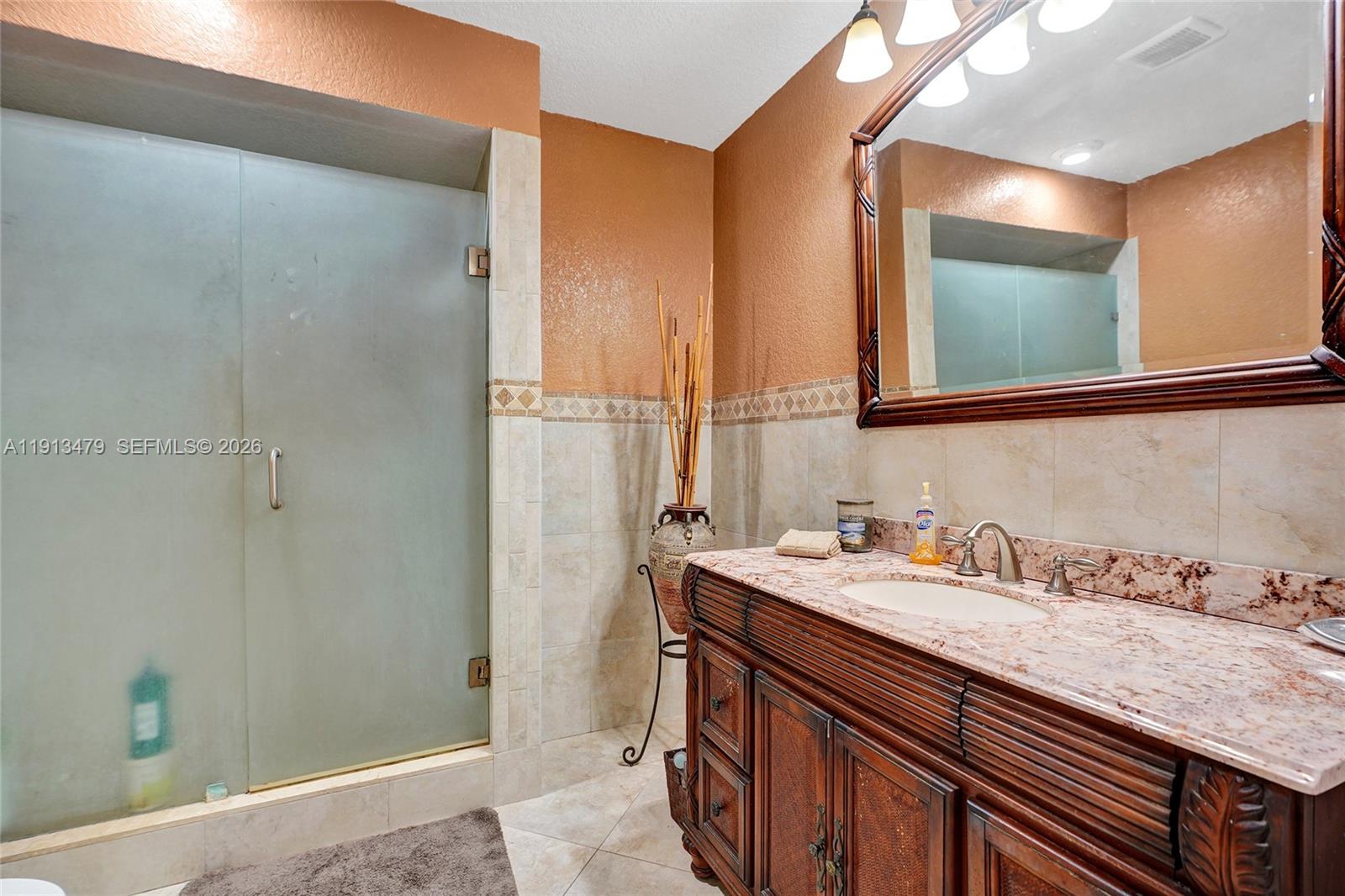 A bathroom features a wooden vanity with a stone countertop, a mirror, and a shower — 311 E 51st St, Hialeah FL 33013, HIALEAH, FL