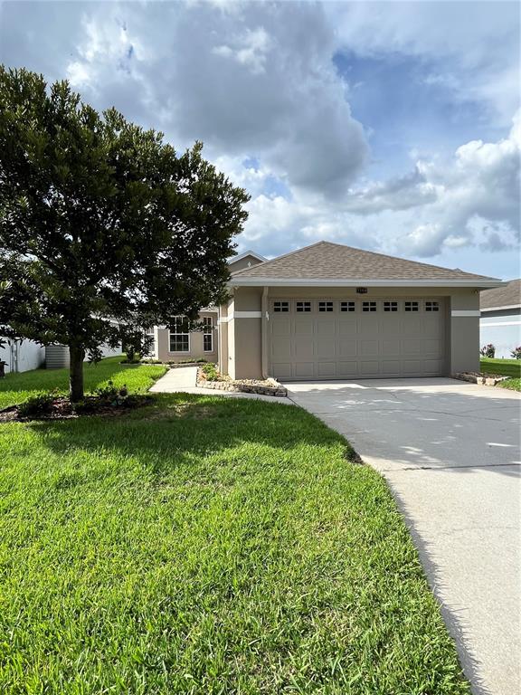 A single-story house with a beige exterior and a two-car garage under a cloudy sky — 2160 SUNSTONE DRIVE, LAKELAND, FL
