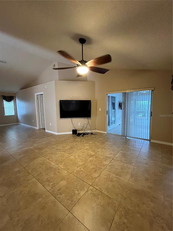 A living room features a vaulted ceiling, a ceiling fan, tile flooring, and sliding doors — 2160 SUNSTONE DRIVE, LAKELAND, FL