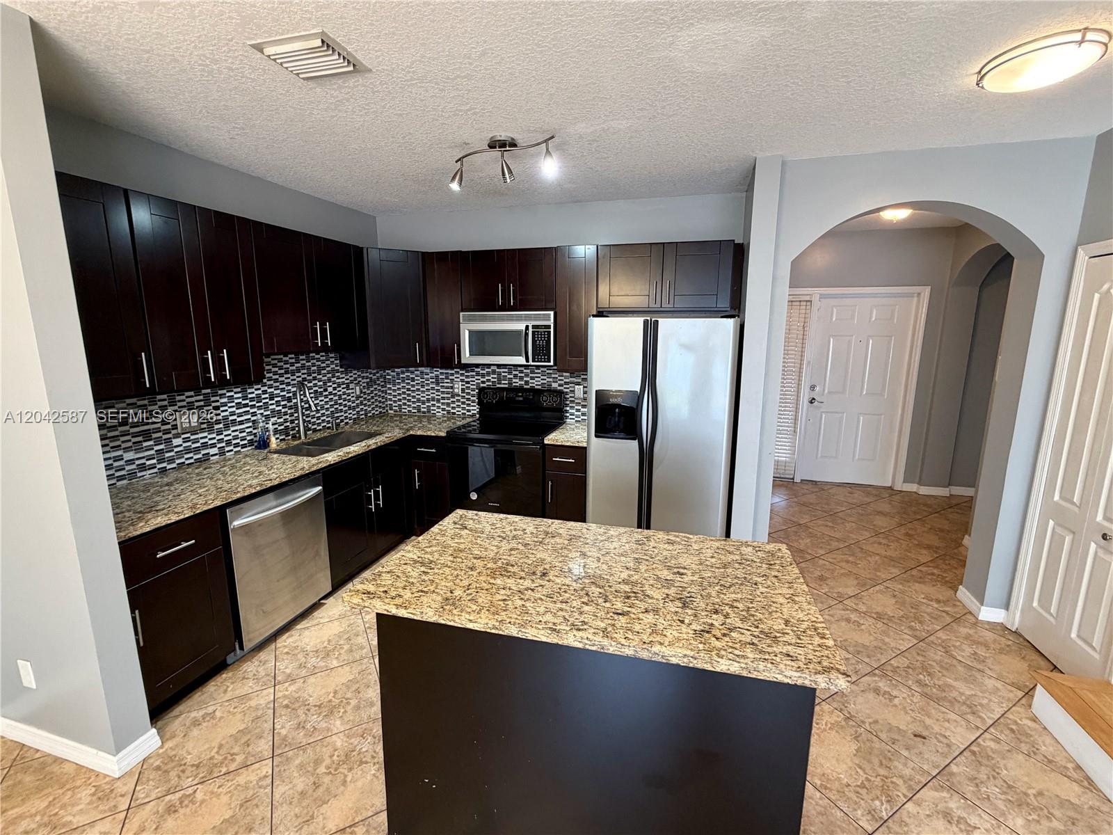 A kitchen features dark wood cabinets, granite countertops, stainless steel appliances, and a central island — 2825 SW 127th Way, Miramar FL 33027, MIRAMAR, FL