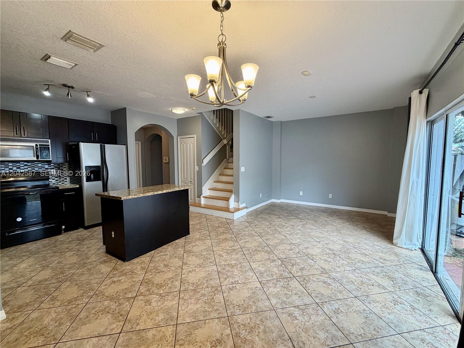 An open-concept kitchen and living area features dark cabinetry, a granite island, and tile flooring — 2825 SW 127th Way, Miramar FL 33027, MIRAMAR, FL