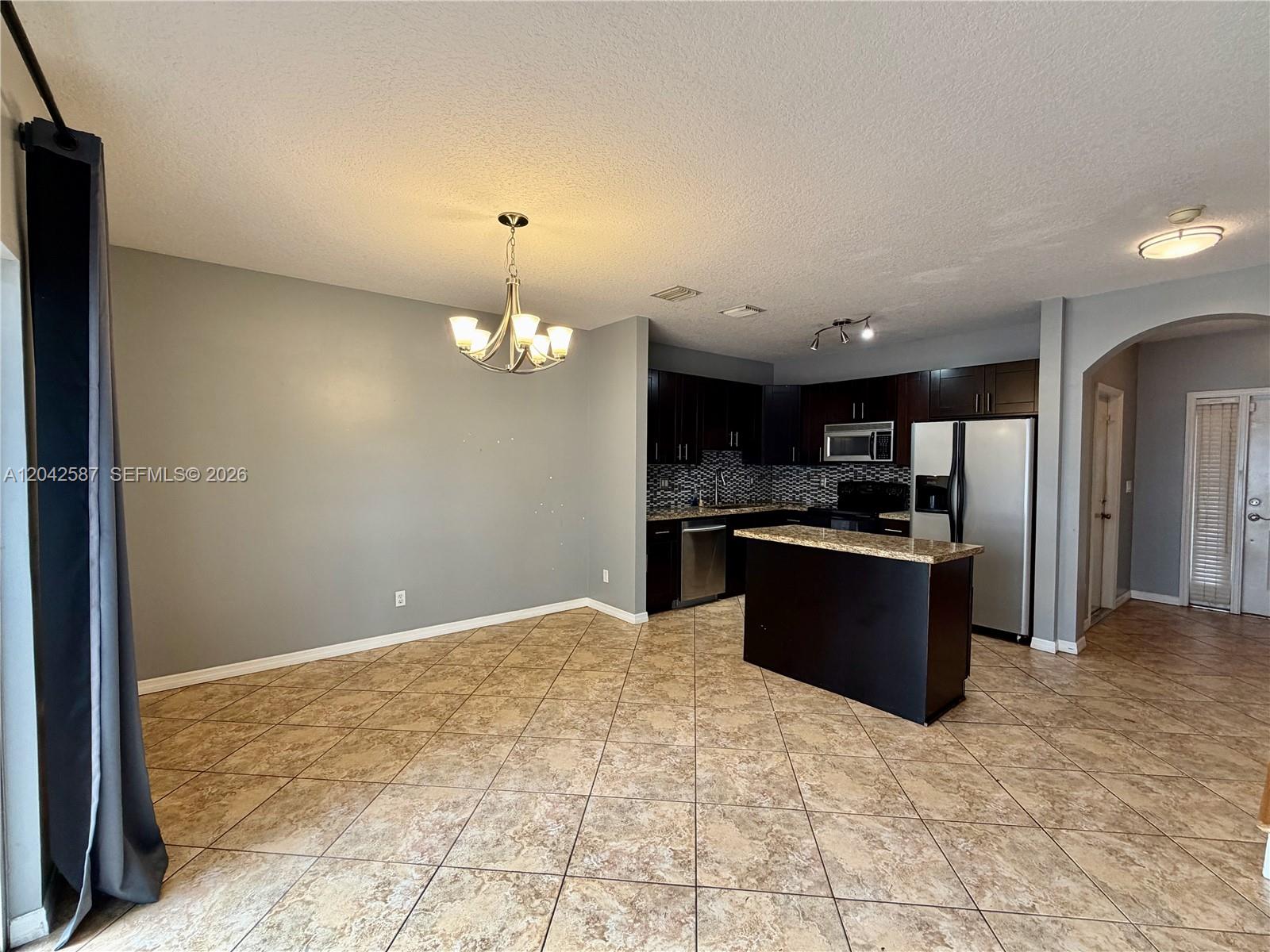 A kitchen with dark cabinets and a central island opens to a tiled dining area — 2825 SW 127th Way, Miramar FL 33027, MIRAMAR, FL