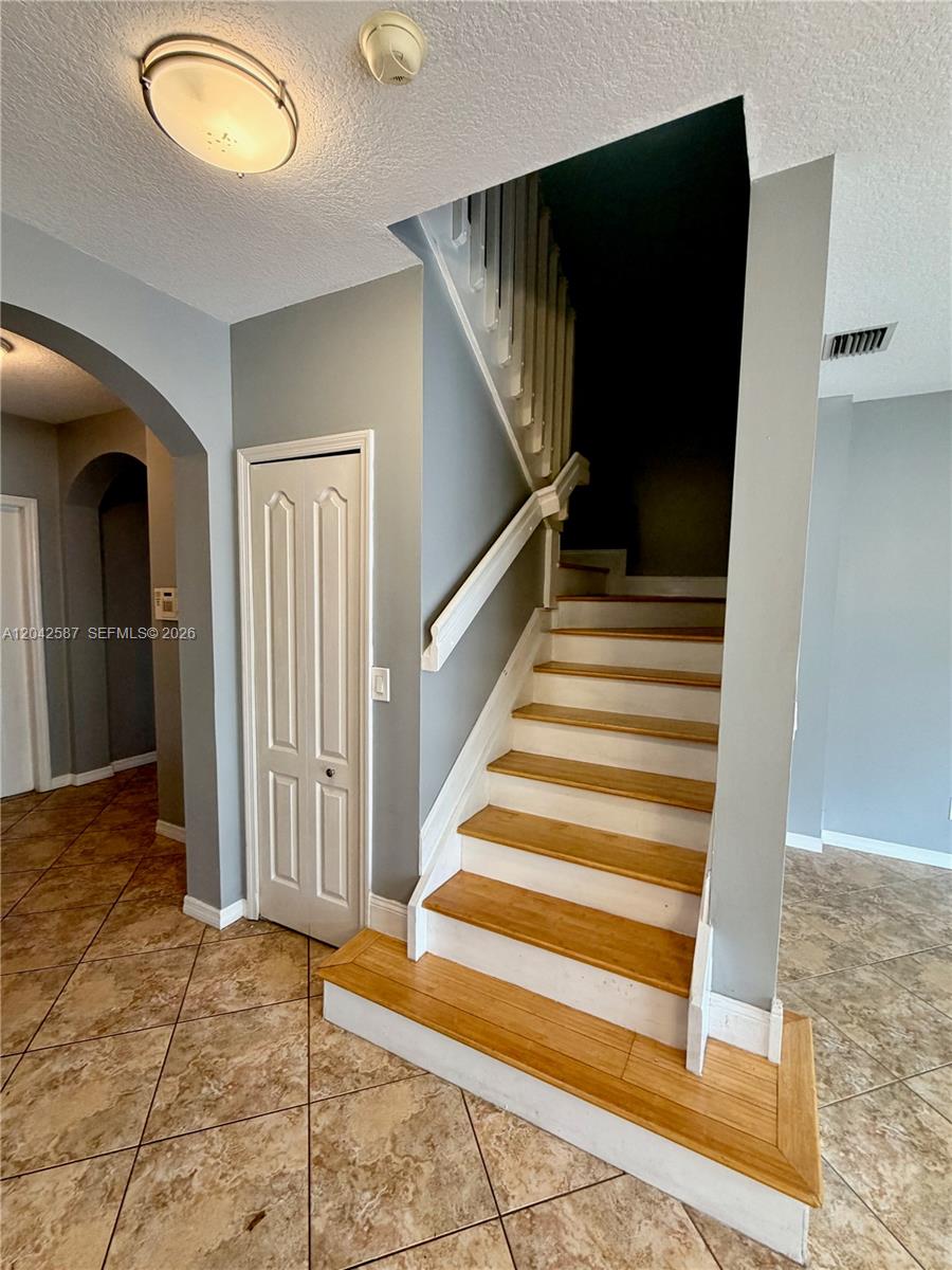 A staircase with wooden treads and white risers sits beside a closet in a tiled foyer — 2825 SW 127th Way, Miramar FL 33027, MIRAMAR, FL