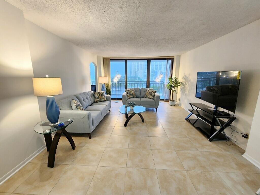 A living room with light tile floors, two grey sofas, a glass coffee table, and balcony — 3400 N Ocean Drive # 703, Riviera Beach FL 33404, RIVIERA BEACH, FL