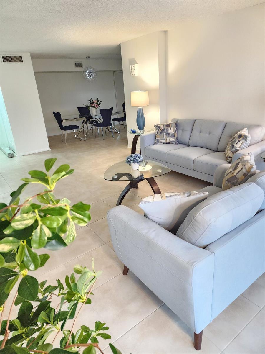 A living room with light gray sofas, a glass coffee table, and an adjacent dining area — 3400 N Ocean Drive # 703, Riviera Beach FL 33404, RIVIERA BEACH, FL