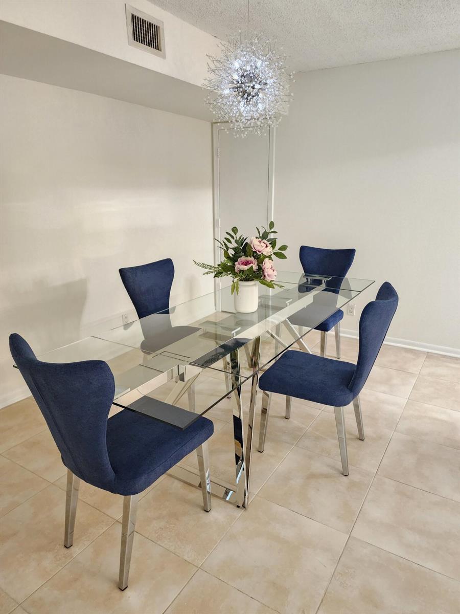 A dining area features a glass table, four blue upholstered chairs, and a crystal chandelier — 3400 N Ocean Drive # 703, Riviera Beach FL 33404, RIVIERA BEACH, FL
