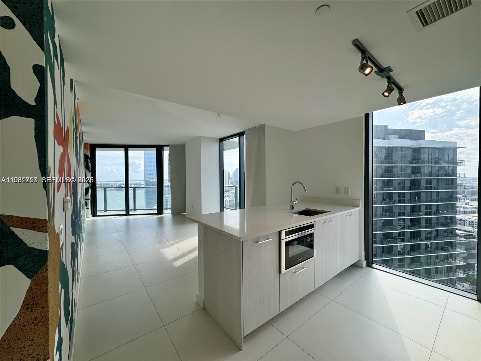 A modern kitchen island with a built-in oven sits in a room with floor-to-ceiling windows — 501 NE 31st St # 3208, Miami FL 33137, MIAMI, FL