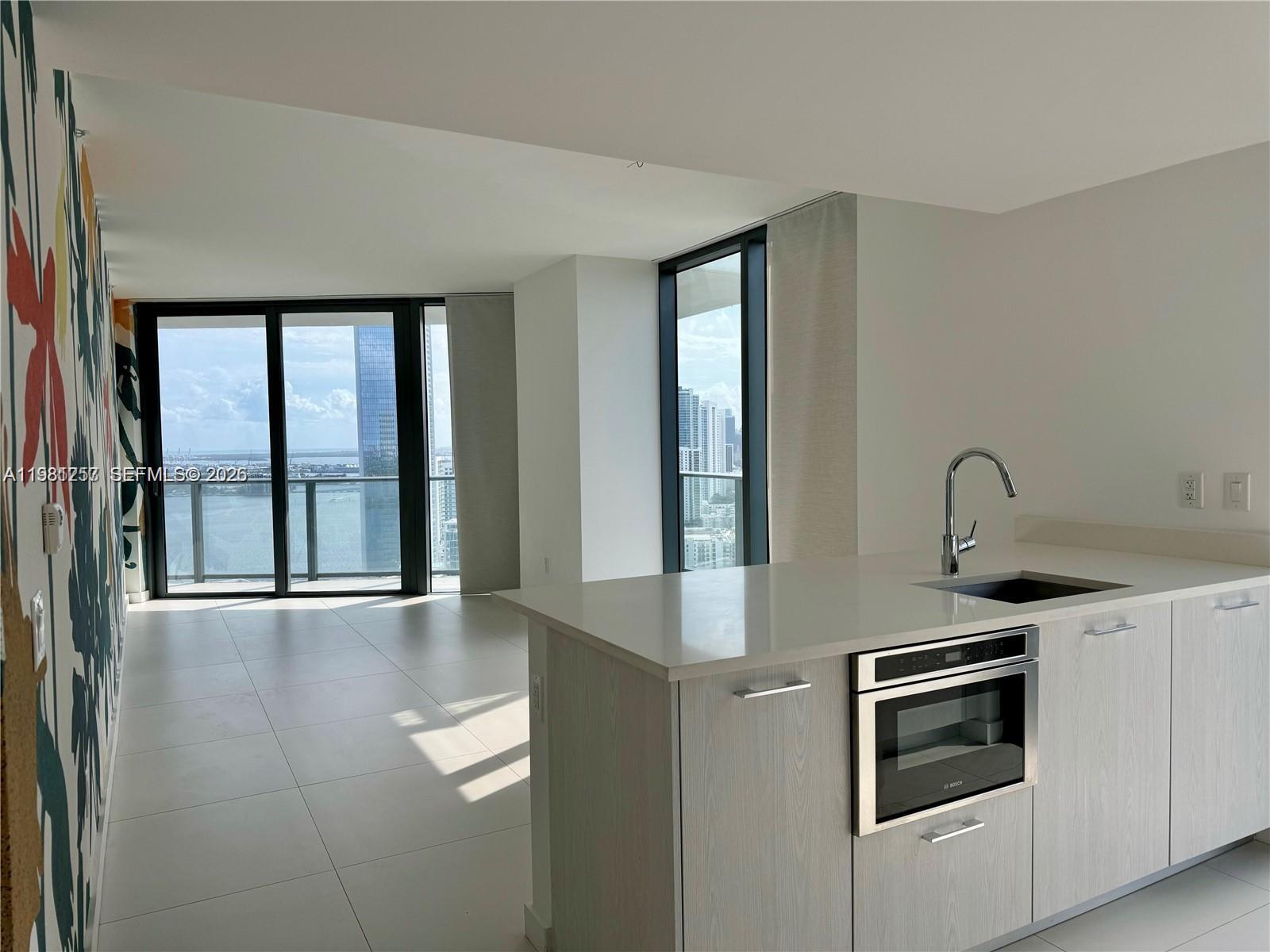 A modern kitchen island with a built-in microwave faces a living area with floor-to-ceiling windows — 501 NE 31st St # 3208, Miami FL 33137, MIAMI, FL