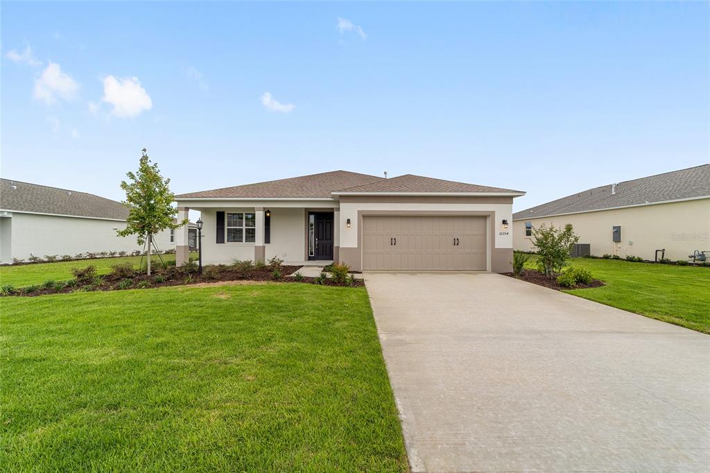A single-story suburban house with a tan exterior, a two-car garage, and a front lawn — 10354 SW 105TH TERRACE, OCALA, FL