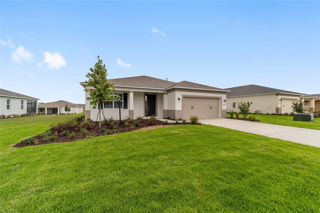 A single-story suburban house with a tan exterior, a two-car garage, and a grassy lawn — 10354 SW 105TH TERRACE, OCALA, FL