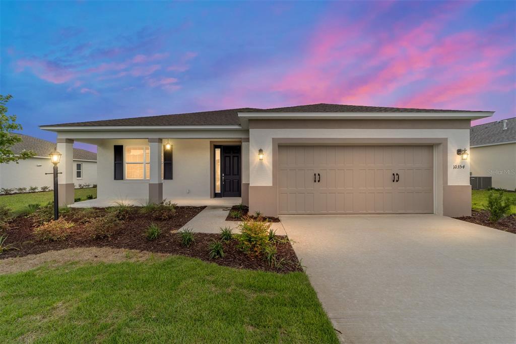 A single-story suburban house with a tan garage, covered porch, and a vibrant sunset sky — 10354 SW 105TH TERRACE, OCALA, FL