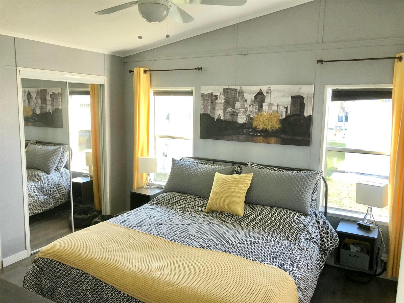 A bedroom with a bed, yellow curtains, city skyline art, and mirrored closet doors — 59012 Captiva Bay, Boynton Beach FL 33436, BOYNTON BEACH, FL
