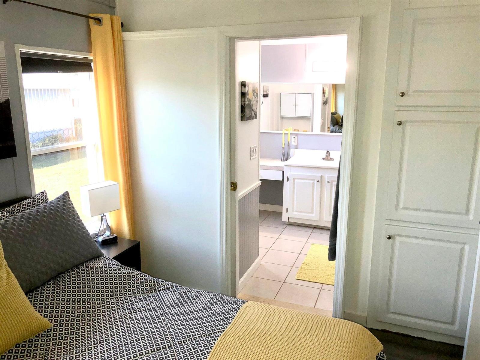 A bedroom with a patterned bedspread and yellow accents leads into a white-tiled bathroom — 59012 Captiva Bay, Boynton Beach FL 33436, BOYNTON BEACH, FL