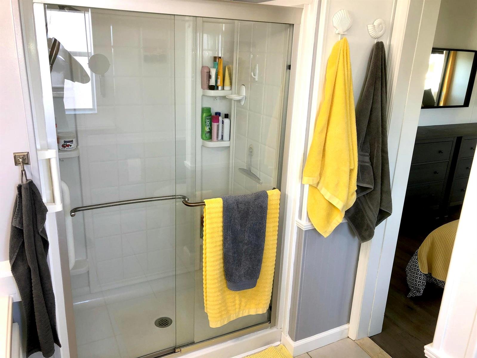 A glass-enclosed shower with white tile walls and hanging towels in a bathroom — 59012 Captiva Bay, Boynton Beach FL 33436, BOYNTON BEACH, FL