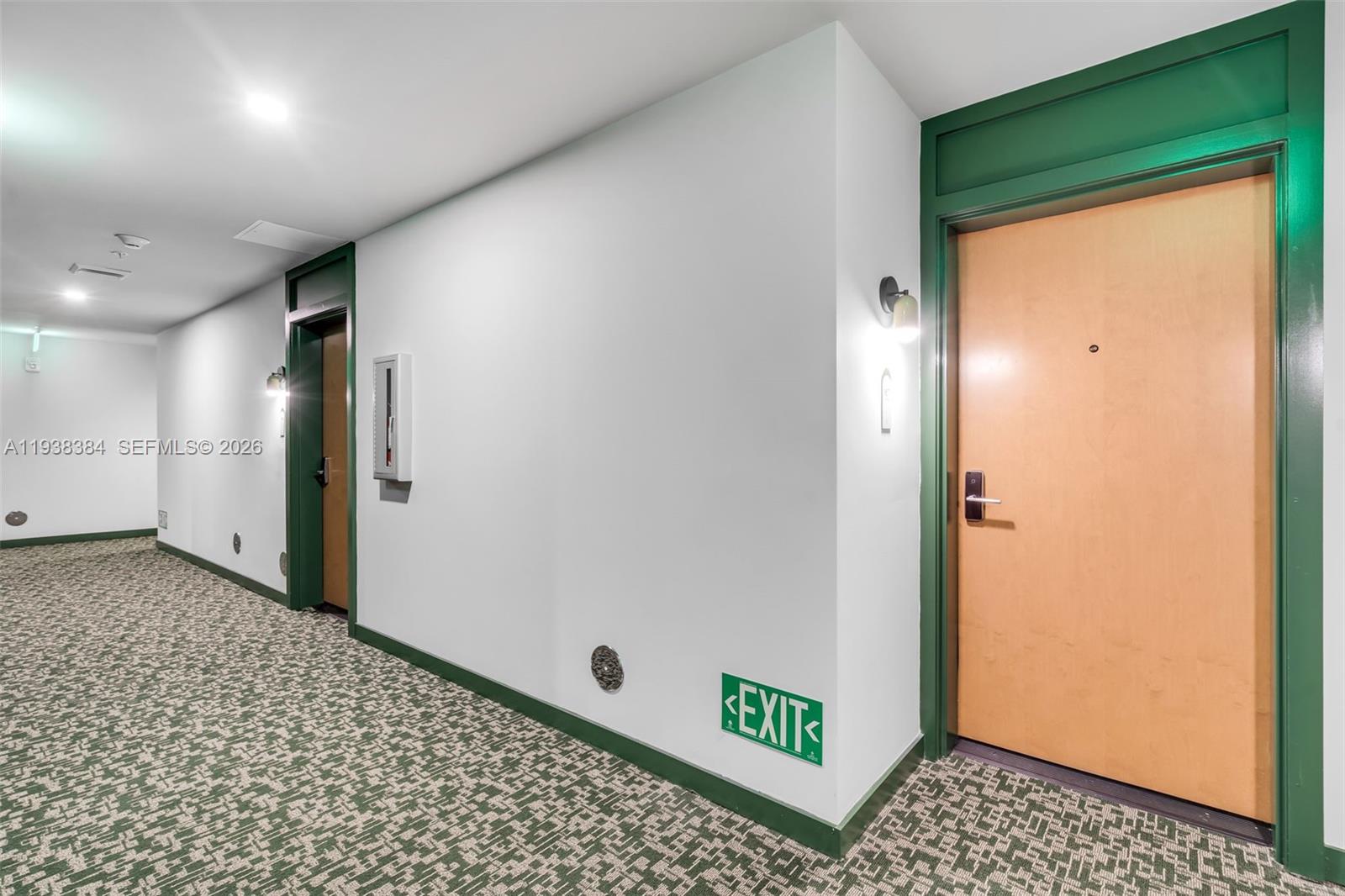 A hallway features green-trimmed doors, patterned carpet, and a low-mounted exit sign on the wall — 11 NE 6th Street # 1607, Miami FL 33132, MIAMI, FL
