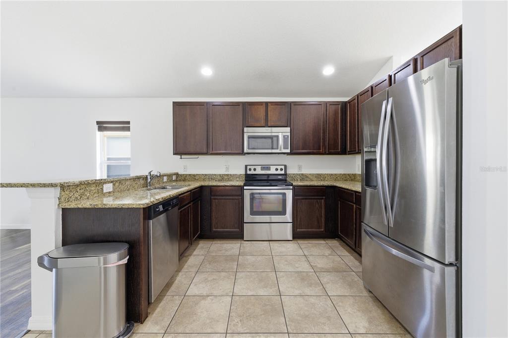 A kitchen with dark wood cabinets, granite countertops, stainless steel appliances, and tile flooring — 248 VICTORY AVENUE, DAVENPORT, FL