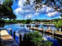 A wooden dock extends into a calm, reflective body of water surrounded by lush greenery — 5072 MONTEGO LANE, PORT CHARLOTTE, FL