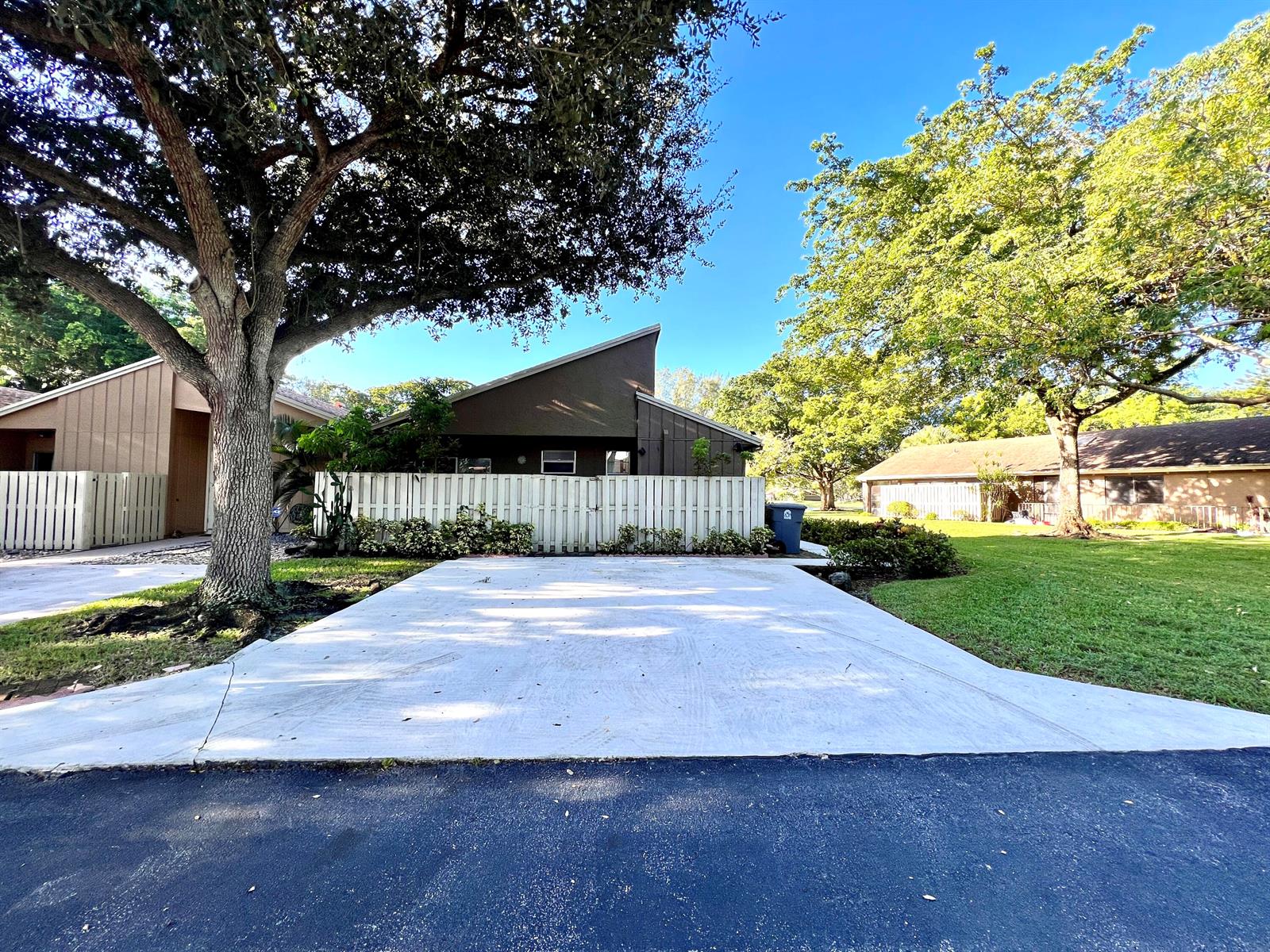 A concrete driveway leads to a house with a white fence and a large tree — 22303 Misty Woods Way, Boca Raton FL 33428, BOCA RATON, FL