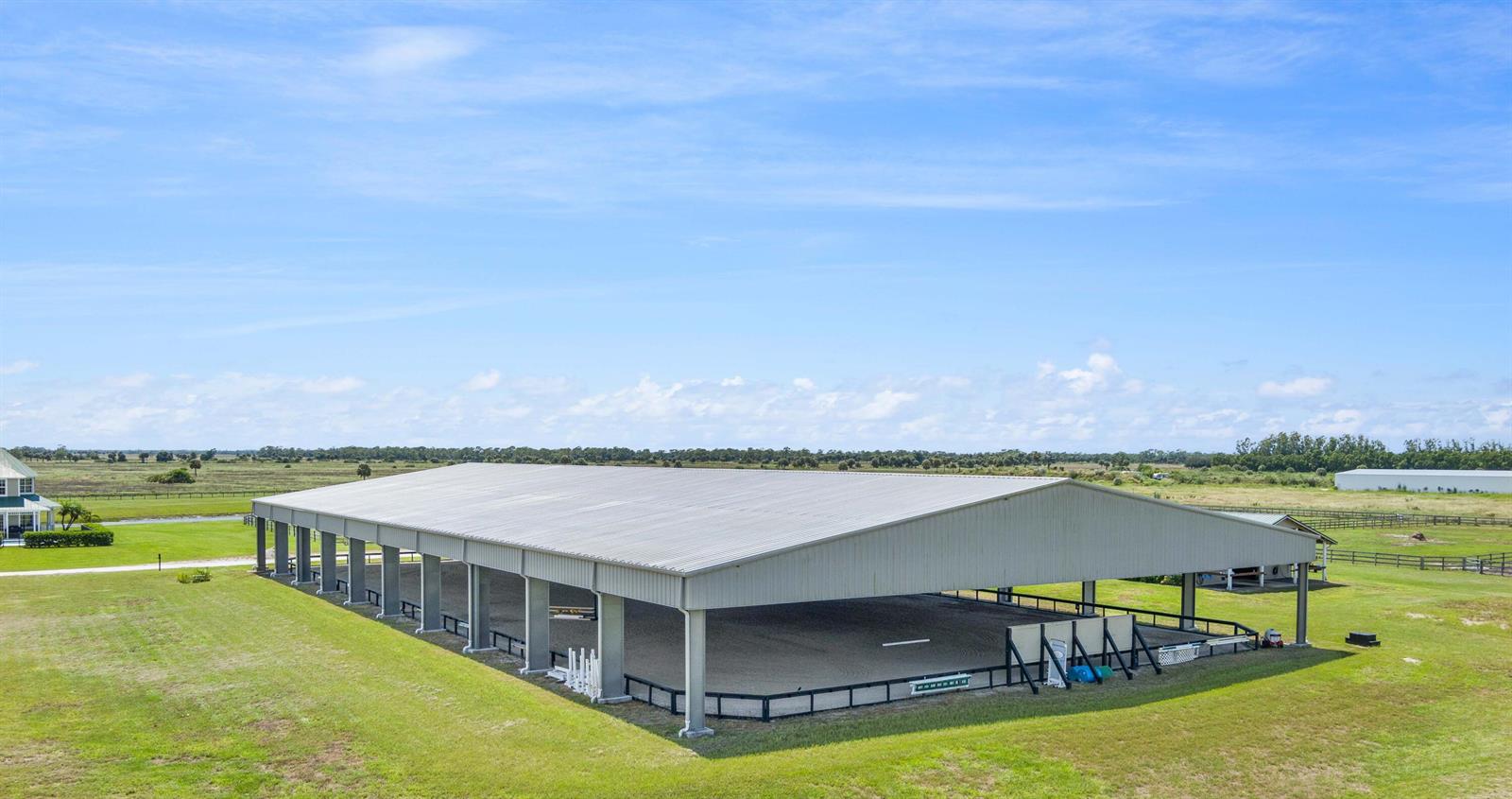 An aerial view shows a large, open-air metal riding arena situated on a grassy field — 13700 SW Groveside Drive, Stuart FL 34997, STUART, FL