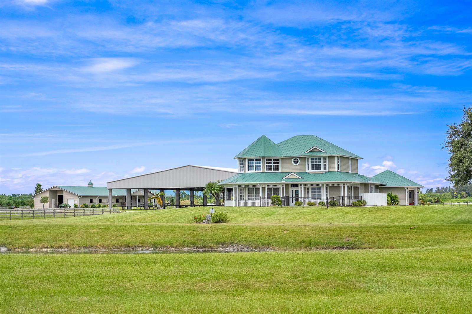 A two-story house with a green metal roof sits on a grassy lawn near barns — 13700 SW Groveside Drive, Stuart FL 34997, STUART, FL