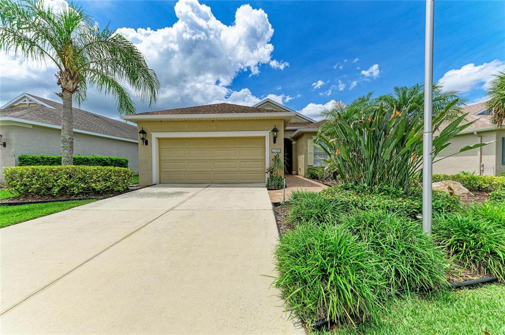 A beige single-story house features a two-car garage, a paved driveway, and tropical landscaping — 11763 FENNEMORE WAY, PARRISH, FL